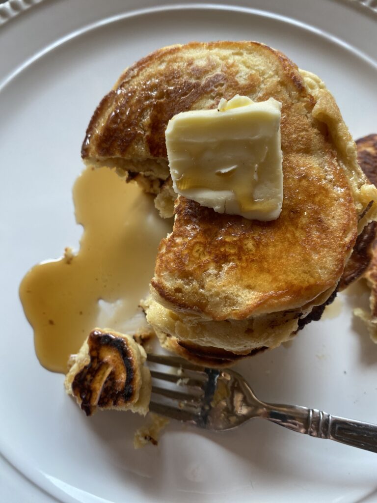 fluffy buttermilk pancakes on a white plate topped with butter and syrup
