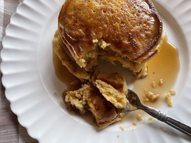 a stack of einkorn pancakes on a white plate topped with maple syrup