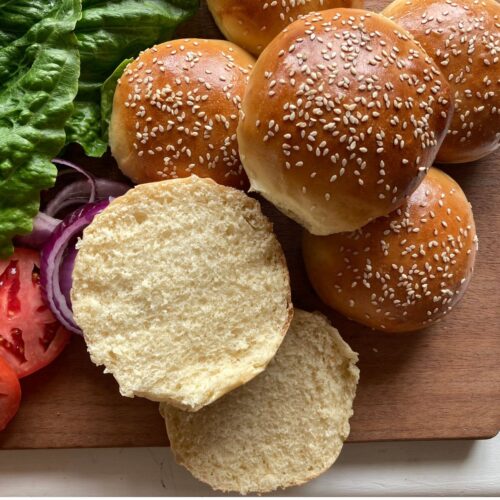 from scratch brioche hamburger buns on a wooden cutting board with lettuce and tomato