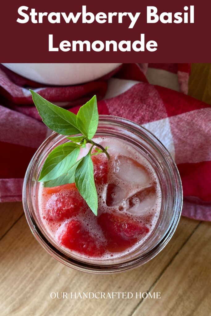 Glass of strawberry basil lemonade with ice and fresh basil garnish, set on a red checkered cloth for a refreshing summer drink.