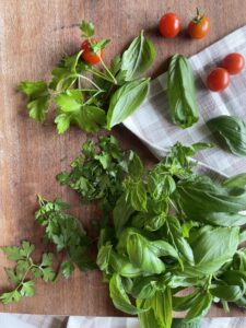 chopped fresh herbs with cherry tomatoes laying on a wooden cutting board