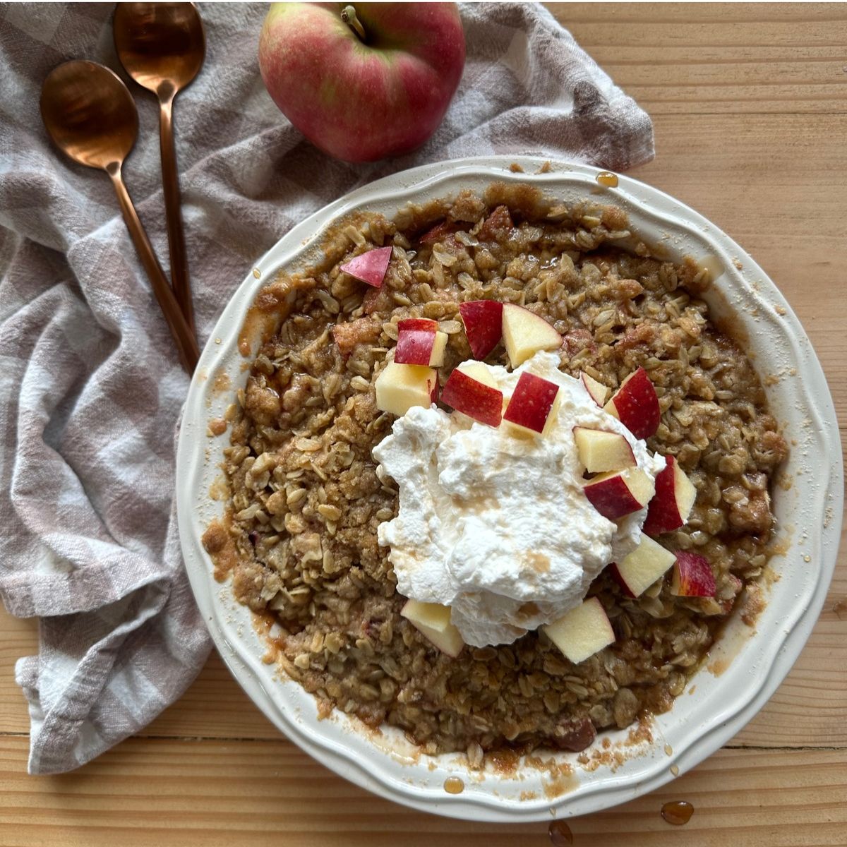 baked einkorn apple crisp topped with a large dollop of whipped cream and chopped fresh apples
