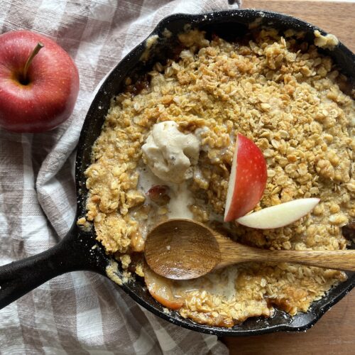 homemade apple crisp with einkorn flour crumble in a cast iron skillet topped with vanilla ice cream