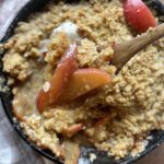 homemade apple crisp with einkorn flour crumble in a cast iron skillet topped with vanilla ice cream