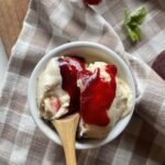 a scoop of homemade vanilla bean ice cream topped with raspberry sauce in a white dish