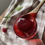 a glass jar of homemade raspberry syrup on a brown and white checkered towel