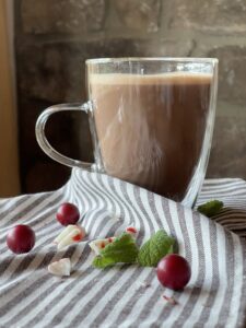 a glass mug of peppermint hot chocolate on a striped towel with red berries