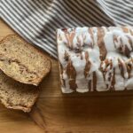 A baked loaf of cinnamon swirl banana bread topped with vanilla icing drizzle.