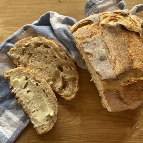 a sliced loaf of baked sourdough bread laying on a wooden countertop