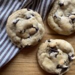 Three sourdough chocolate chip cookies laying on a wooden cutting board