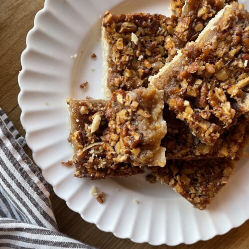 Pecan pie bars cut into small squares stacked on a white plate