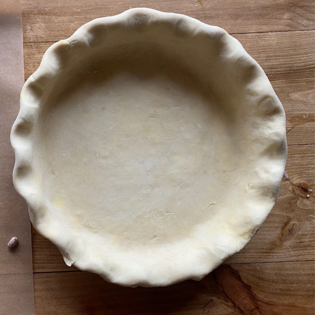 Unbaked sourdough pie crust in a fluted edge pattern, placed in a pie dish on a wooden surface.