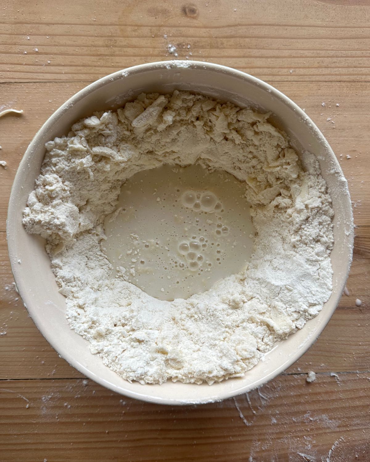 a large mixing bowl full of flour, with a well in the center. A water and sourdough starter mixture has been poured into the well