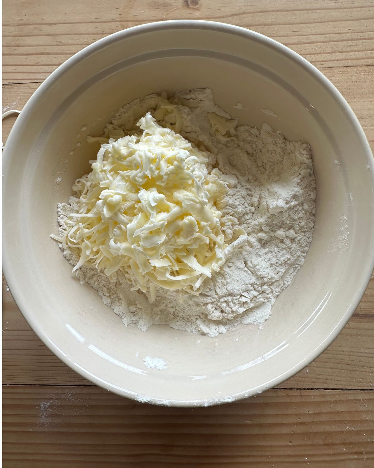 a large mixing bowl full of flour, with grated butter on top