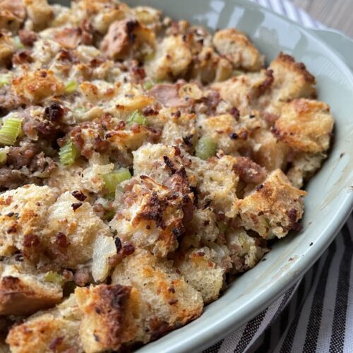 A pan of baked sourdough bread stuffing with sausage, sauteed veggies, and herbs
