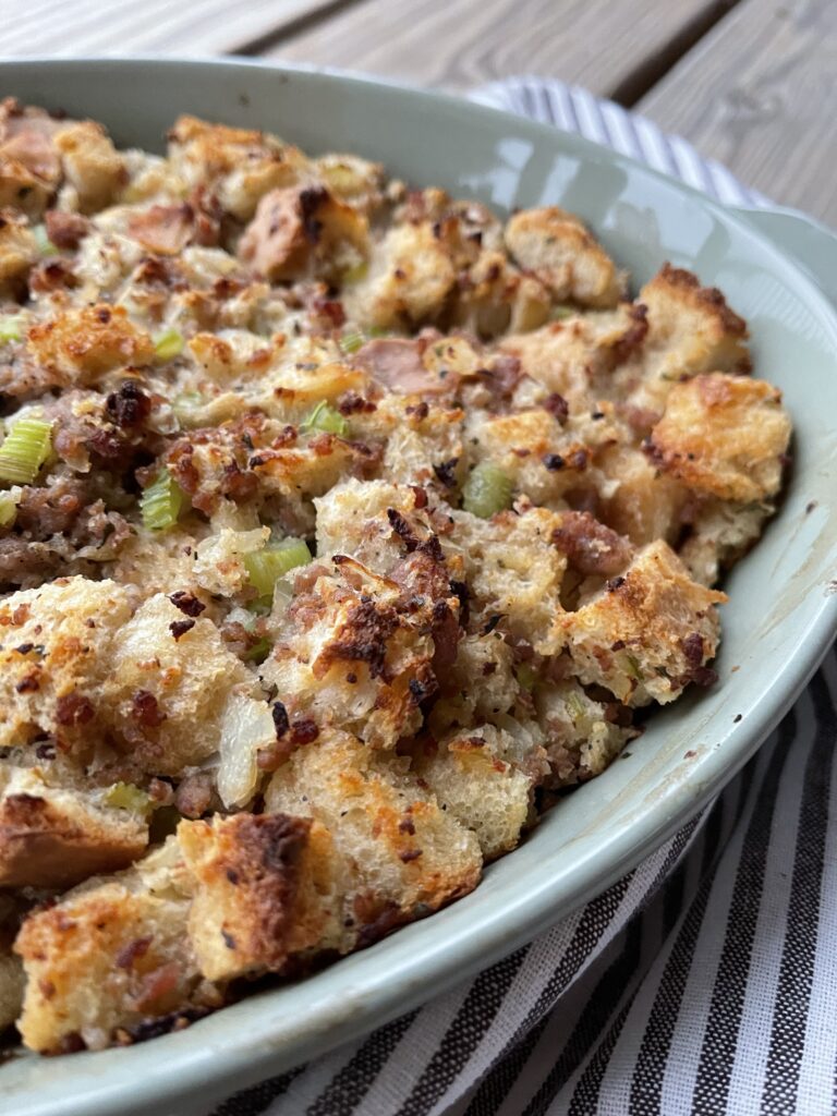 A pan of baked sourdough bread stuffing with sausage, sauteed veggies, and herbs