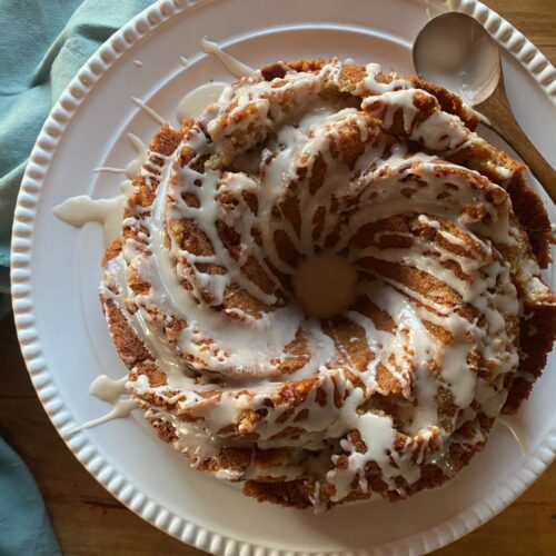 sourdough discard coffee cake on a white stand drizzled with vanilla icing