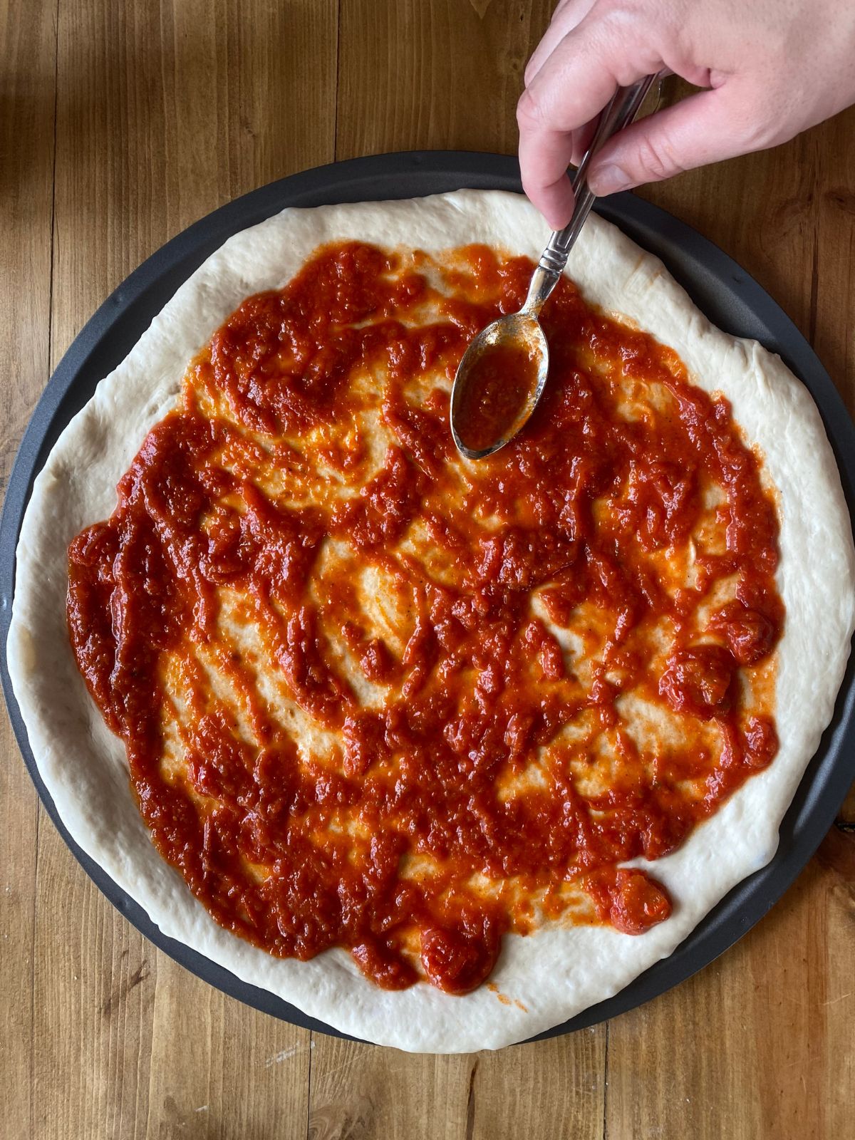 pizza sauce is being spread onto a large pan of unbaked pizza crust
