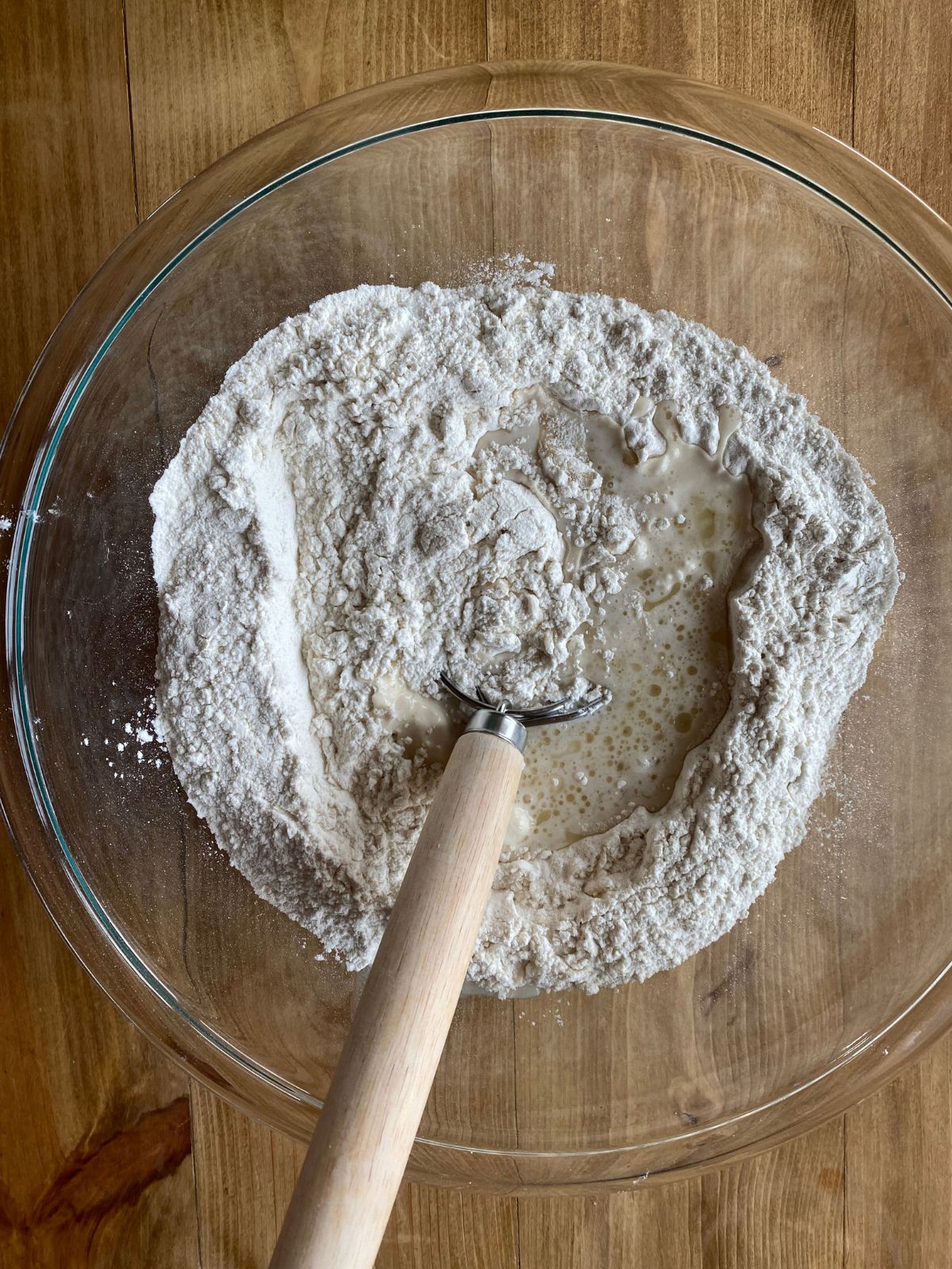 a bowl of sourdough discard pizza dough, with a wooden spoon stirring the dough