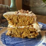 a slice of sourdough carrot cake with cream cheese frosting on a blue and white plate