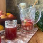 a glass pitcher of flavored water kefir with a small glass jar sitting to the sit full of water kefir