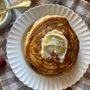 a stack of sourdough discard pancakes on a white plate topped with butter and syrup
