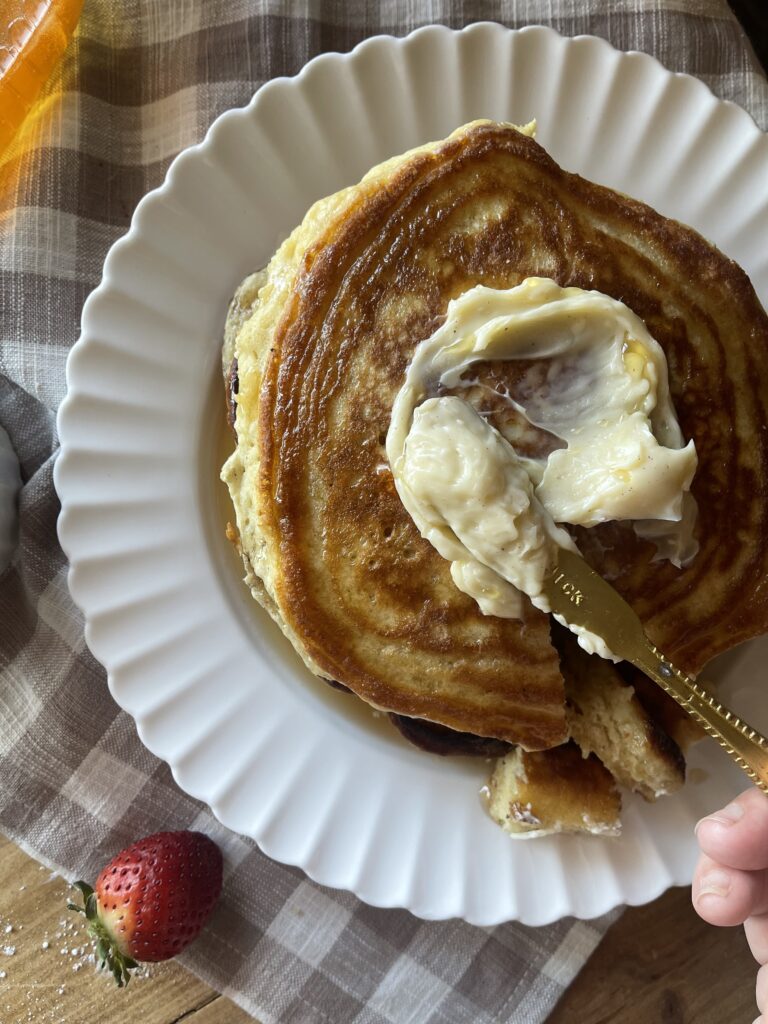 a stack of sourdough discard pancakes on a white plate topped with butter and syrup