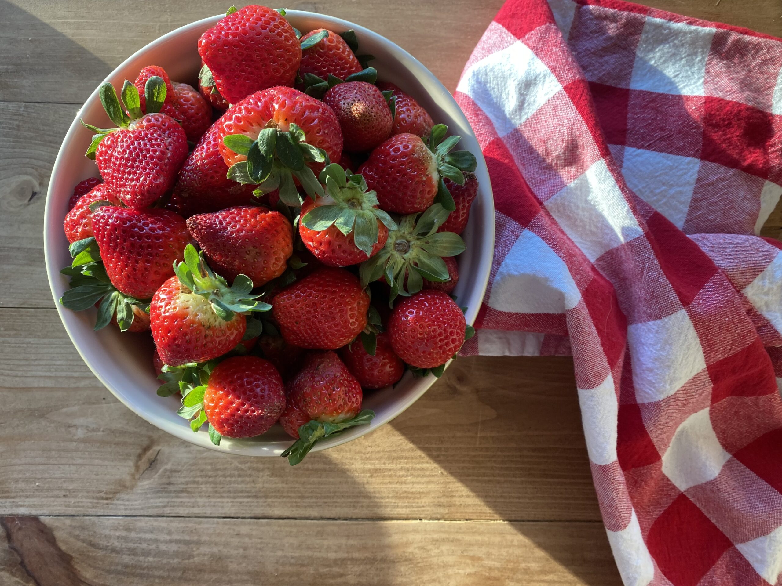 a bowl of strawberries on a wooden tabletop with a red and white checkered towel