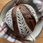 a loaf of sourdough chocolate bread in a white Dutch oven. A striped towel lays underneath the loaf
