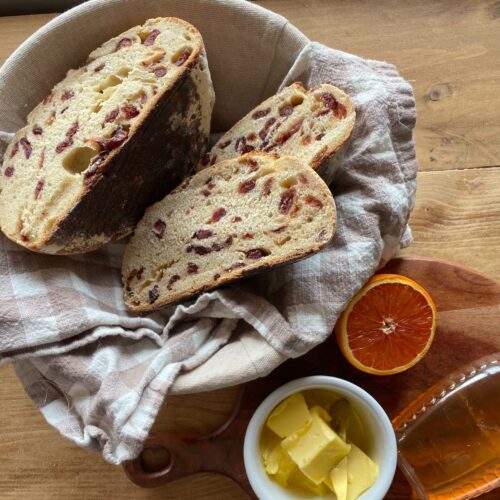 a sliced loaf of orange cranberry sourdough bread in a bowl with sliced butter on the side