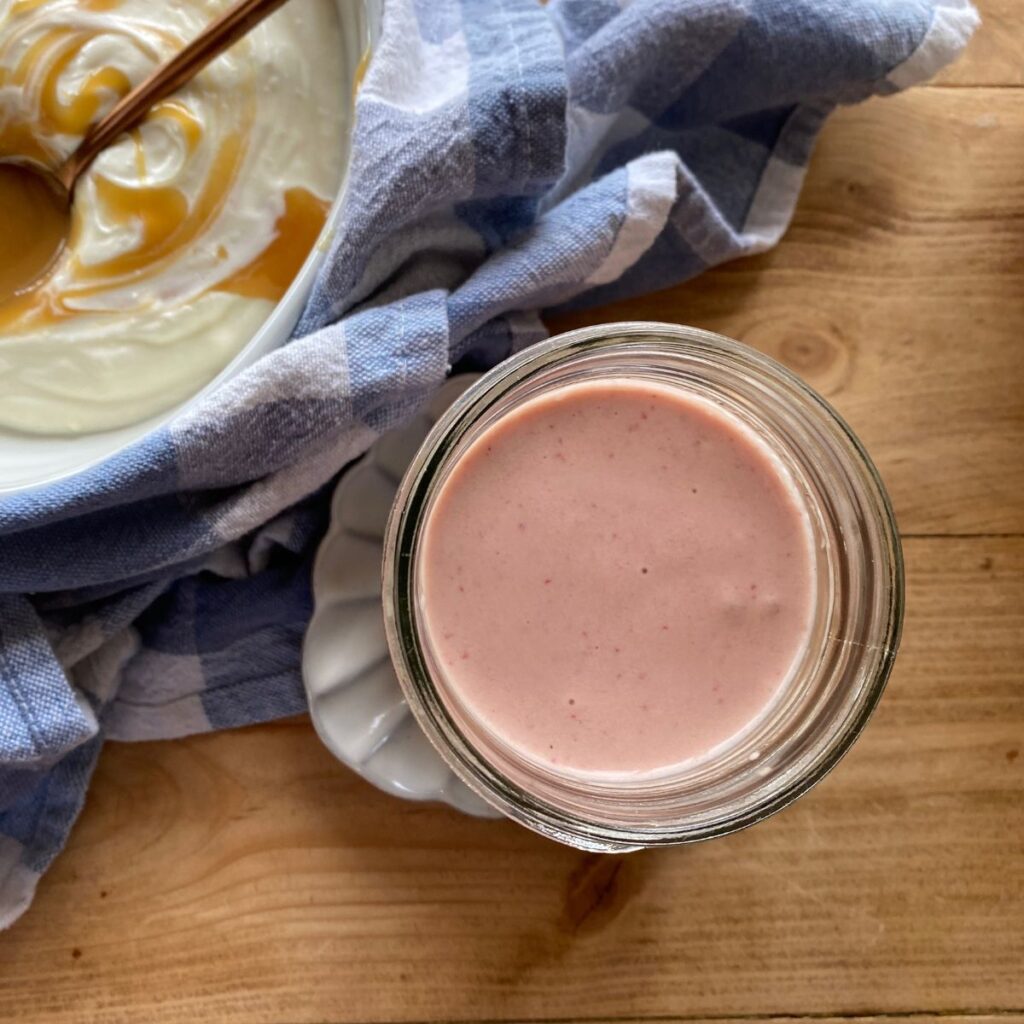 Strawberry banana Greek yogurt smoothie in a glass jar, set on a wooden table with a blue and white checkered cloth in the background