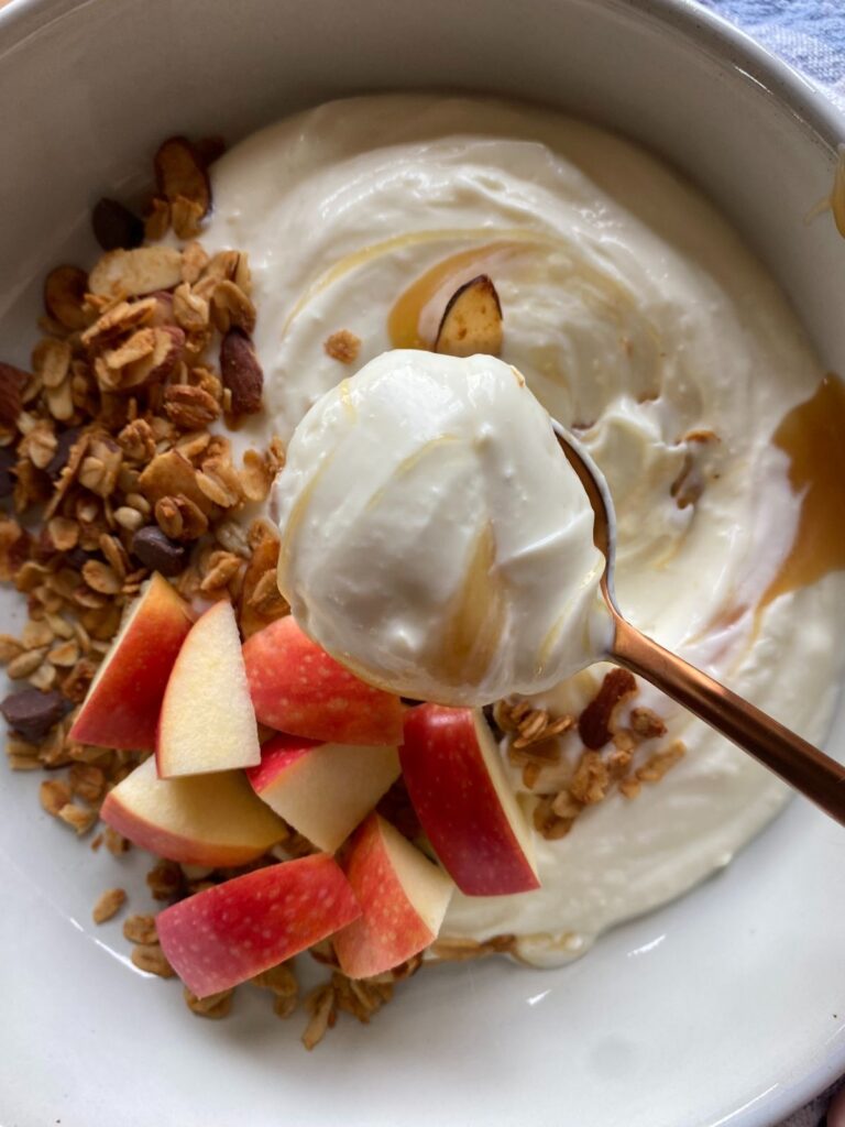 Close up view of a bowl of Greek yogurt topped with apple slices, granola, and a drizzle of honey.