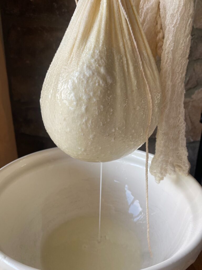 Straining homemade Greek yogurt in cheesecloth over a ceramic bowl to remove whey and thicken the texture.