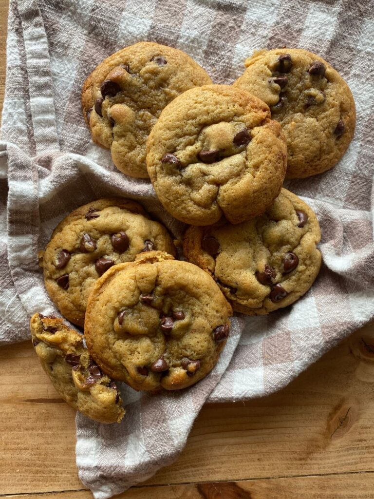 Soft and gooey brown butter sourdough chocolate chip cookies, surrounded by more golden-brown cookies on a linen cloth background.