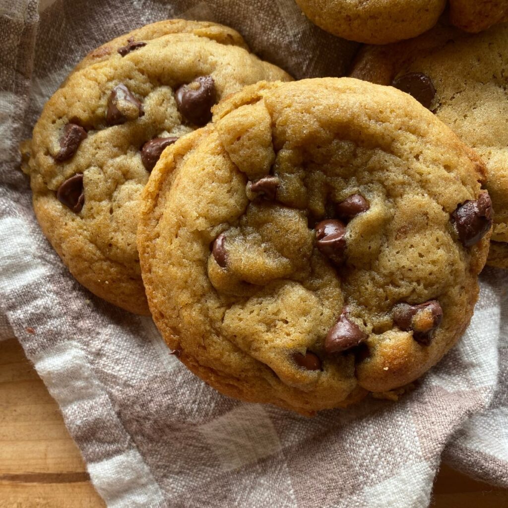 a close of view of a baked sourdough chocolate chip cookie laying on a checkered towel