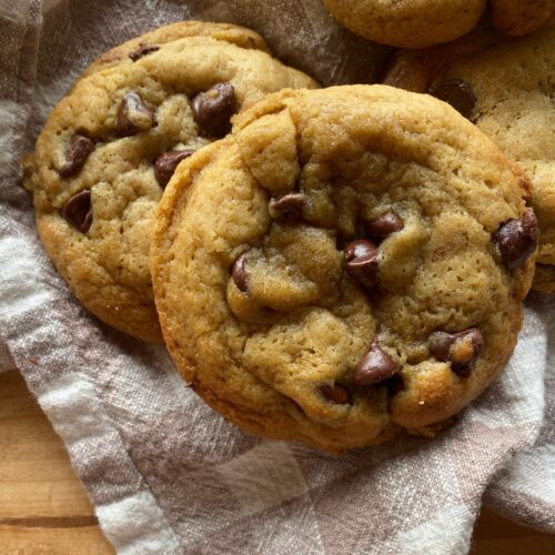 a close up view of a baked sourdough chocolate chip cookie laying on a checkered towel