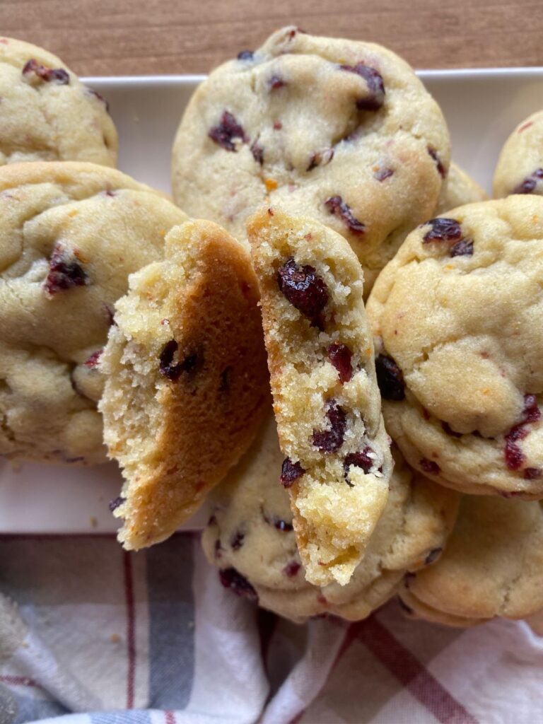 Soft and chewy orange cranberry cookies filled with dried cranberries and orange zest, stacked on a white plate over a rustic wooden table.