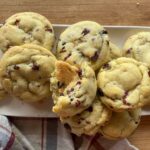 Soft and chewy orange cranberry cookies filled with dried cranberries and orange zest, stacked on a white plate over a rustic wooden table.
