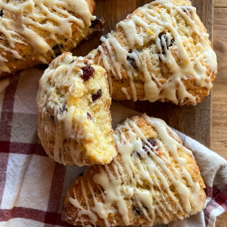 baked orange cranberry scones drizzled with icing and arranged on a wooden cutting board