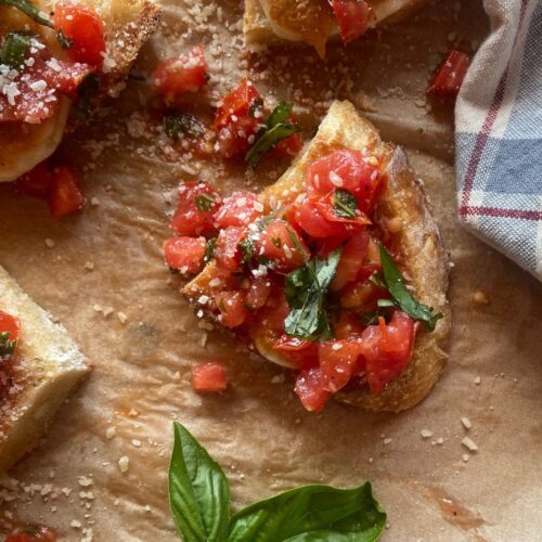 Close-up of homemade sourdough bruschetta topped with fresh diced tomatoes, basil, garlic, and a sprinkle of Parmesan on toasted sourdough bread, served on parchment paper.