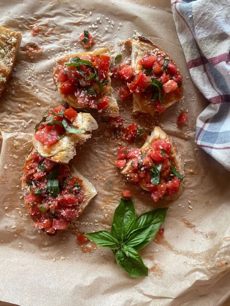 Homemade sourdough bruschetta topped with fresh diced tomatoes, basil, garlic, and a sprinkle of Parmesan on toasted sourdough bread, served on parchment paper.