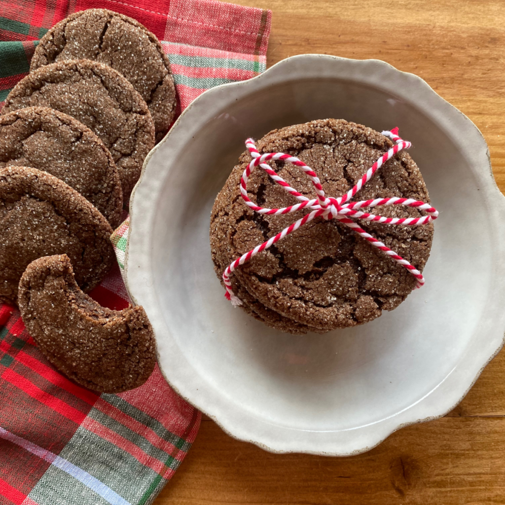 Stack of chocolate brownie crinkle cookies tied with red and white string on a plate, with more cookies and a festive plaid napkin in the background.