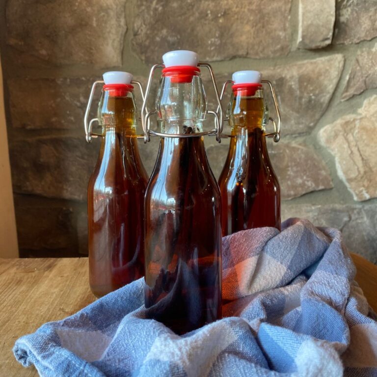 Homemade bourbon vanilla extract in glass swing-top bottles with a blue kitchen towel, set against a rustic stone background.