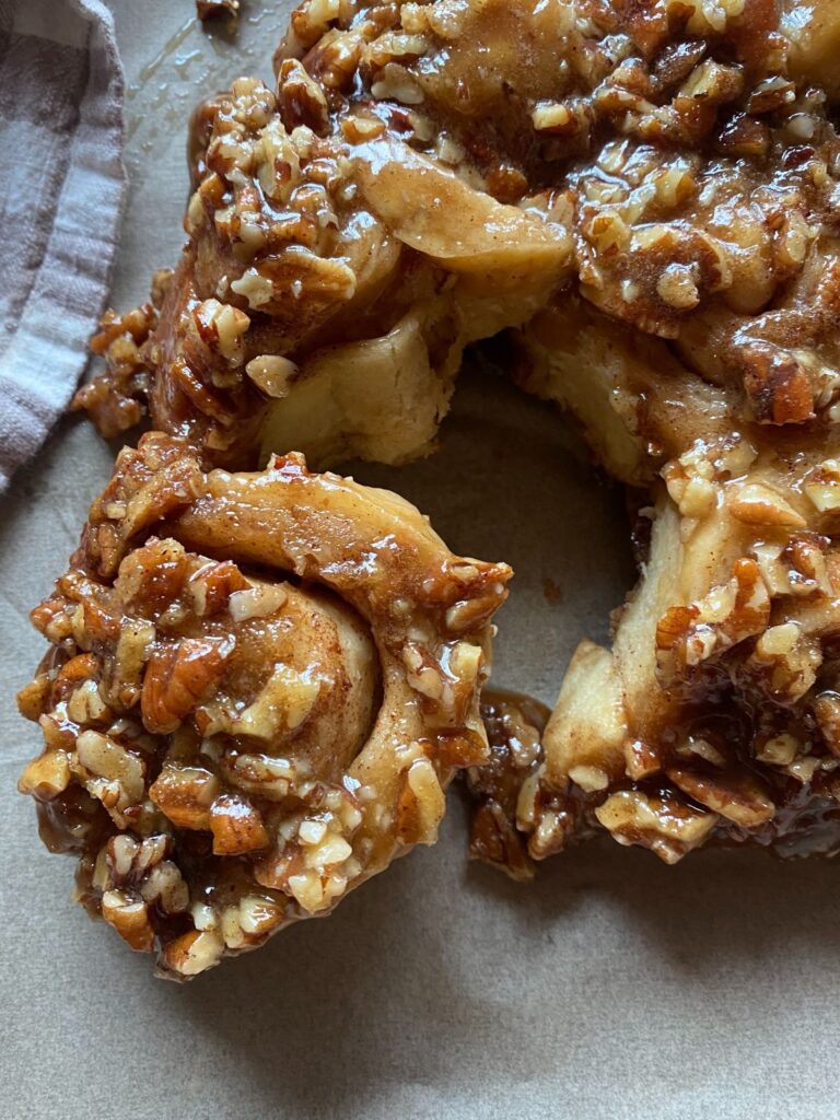 Close-up of homemade sourdough sticky buns topped with caramelized pecans and rich cinnamon glaze.