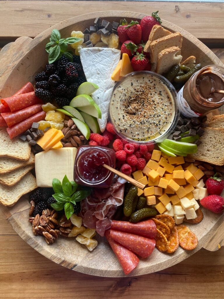 Holiday charcuterie board with assorted cheeses, cured meats, fresh fruit, nuts, toasted bread slices, and a jar of red raspberry jam.