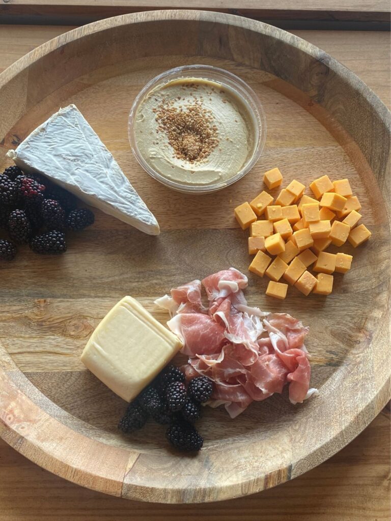 a wooden serving tray with assorted cheeses, meats, hummus, and berries