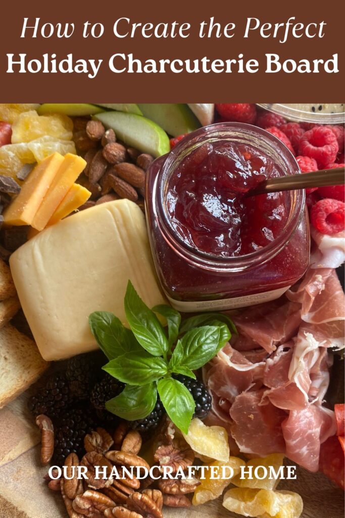 Holiday charcuterie board with assorted cheeses, cured meats, fresh fruit, nuts, toasted bread slices, and a jar of red raspberry jam. Text overlay reads "How to Create the Perfect Holiday Charcuterie Board."