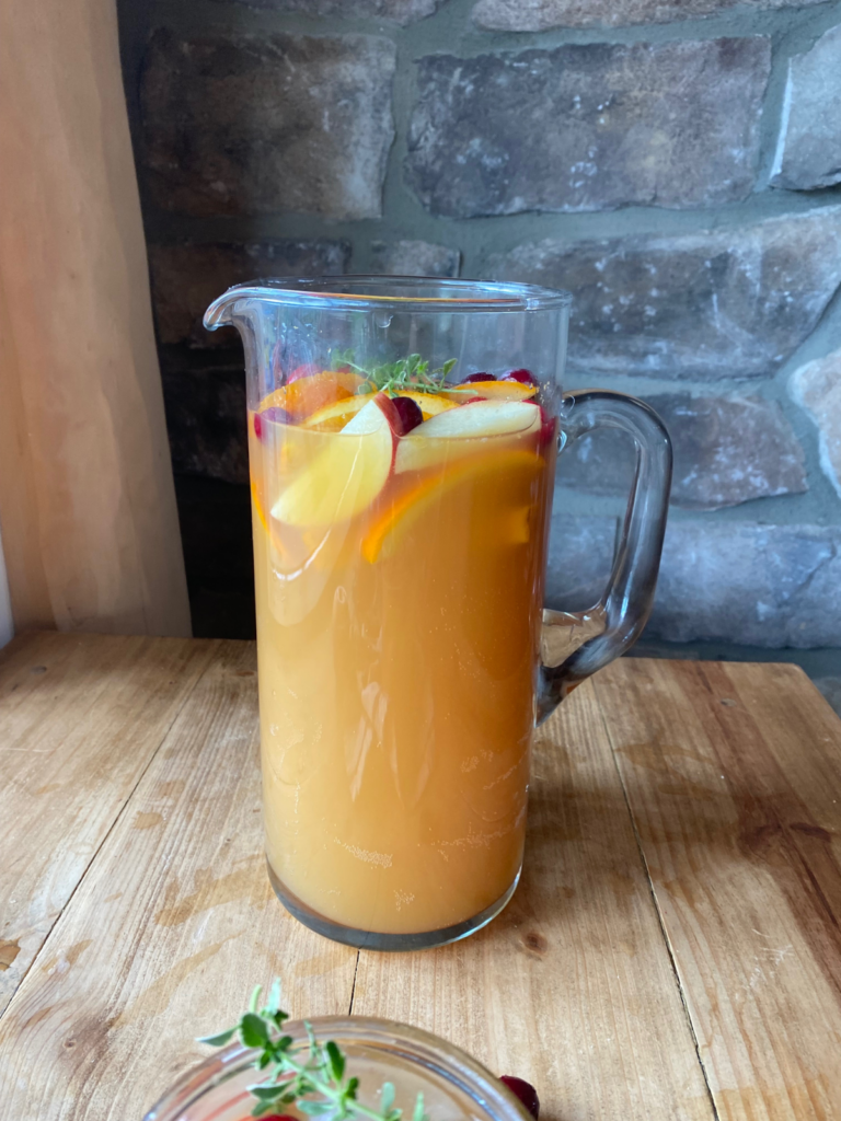 A large glass pitcher filled with homemade apple cider punch. It is topped with seasonal sliced fruit