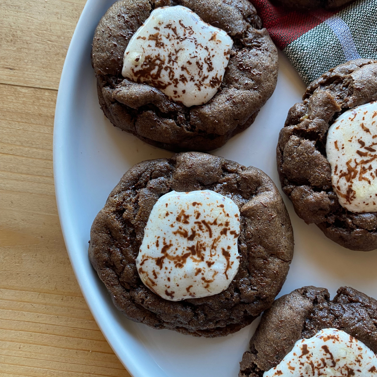 Soft and chewy hot chocolate cookies topped with toasted marshmallows on a white plate — a cozy winter dessert perfect for holiday baking.