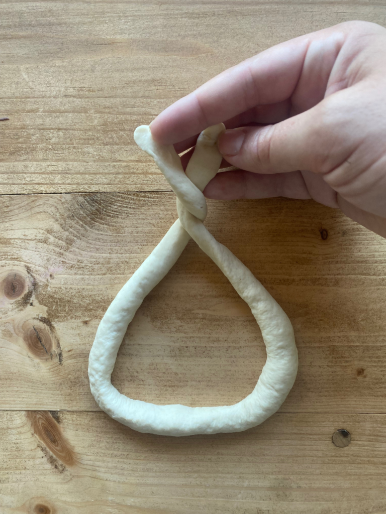 a long rope of sourdough pretzel dough being twisted and shaped into a soft pretzel